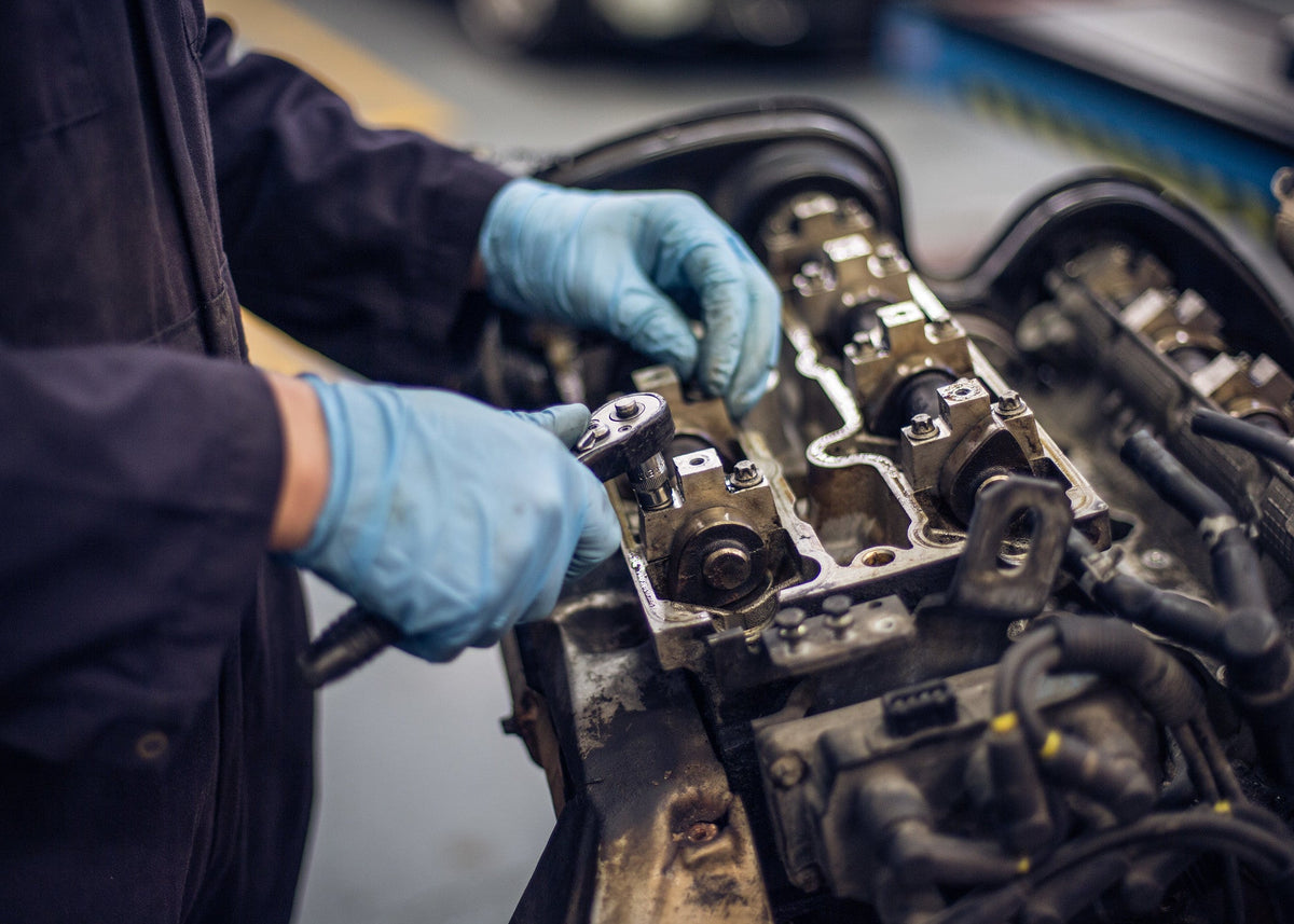 Person working on a car engine with blue gloves