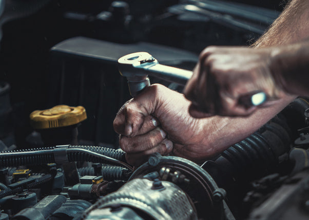 Person working on a car engine with a wrench